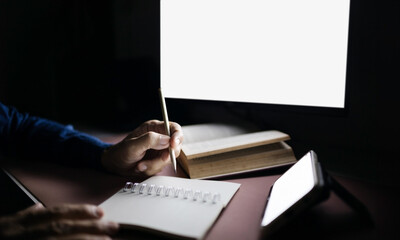 Close-up shot, person's hand using desktop computer work with mobile and taking note at night time