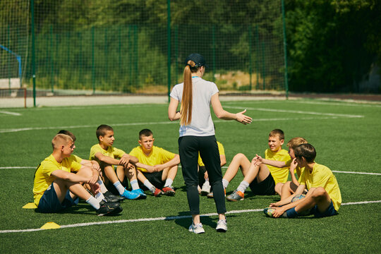 Youth Sports Education. Group of enthusiastic young soccer players listening to strategic advice from female coach, focusing on teamwork and skill development. Sport, school, active lifestyle concept - Powered by Adobe