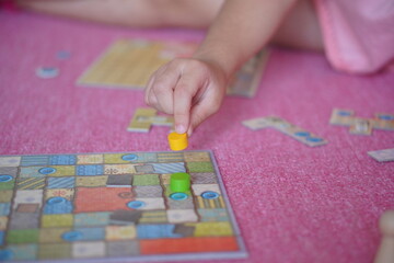 Obraz premium 小学生の子供がボードゲーム遊びを楽しんでいる様子。駒を動かしている手元。