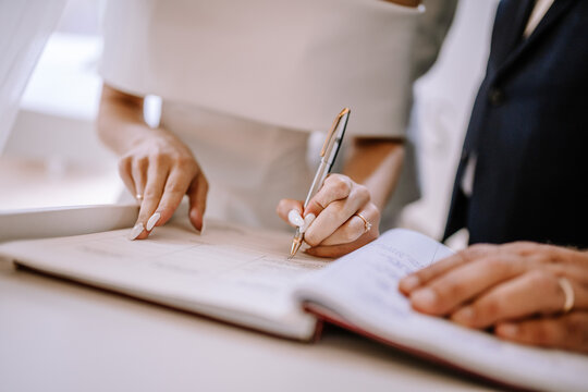 Valmiera, Latvia - September 9, 2023 - Bride signing the wedding register during the ceremony, showcasing a close-up of her hands with a pen and detailed manicured nails.