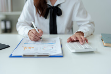 Asian female freelancer sitting and working with laptop doing paperwork, calculations, recording business information online at your desk in your home office. Success concept modern entrepreneur.