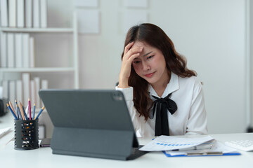 Tired businesswoman having a headache in modern office Creative woman working at office desk Casual female office worker Feeling a headache while working hard on a laptop computer.