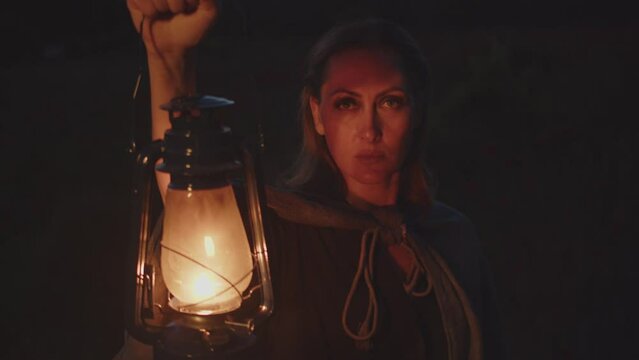 A woman with a kerosene lamp in her raised hand illuminates her face in the dark