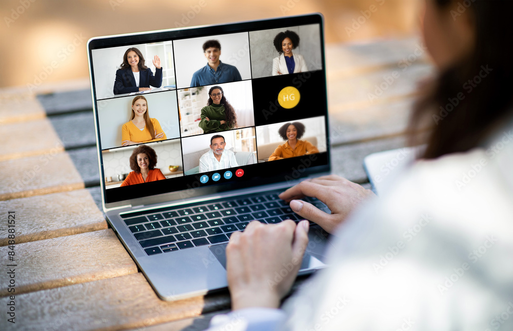 Poster unrecognizable woman sitting at a desk, typing on a laptop while video conferencing with a diverse g