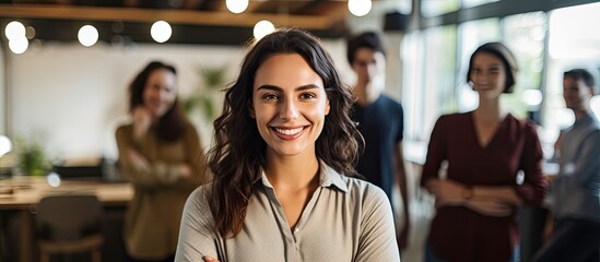 A young professional businesswoman smiling in a coworking space is shown in a portrait with her team looking at the camera with a creative office background and copy space image - Powered by Adobe