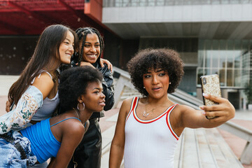 Latin woman takes selfie with her girlfriends on building stairs in the city.
