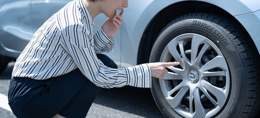 車のタイヤを見て気にする女性 © ponta1414