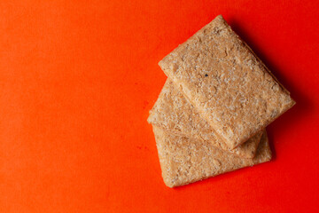 Stacked Indian mithai (dessert), delicate, soft, crunchy Gajak Bars made of Til, Desi Ghee, and Jaggery, on an orange background. Top view.