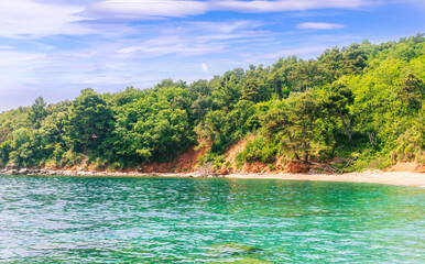 scenic summer landscape of beautiful sea shore with water vawes in bay, green forest on isle rock and nice cloudy sky on background