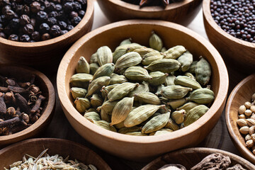 Whole seeds of warming Indian spice cardamom in wooden bowl close-up, ayurvedic treatment, alternative medicine