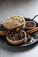 Set of whole warming Indian spices in wooden bowls on a gray background vertical