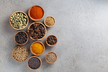 A variety of spices in wooden bowls on a gray background with copyspace top view, vibrant colors and textures.