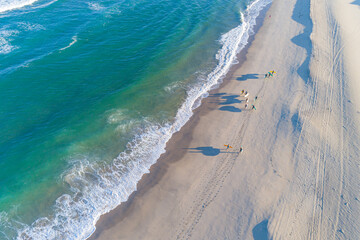 surfers on the shore of a beach at sunrise as seen from a drone