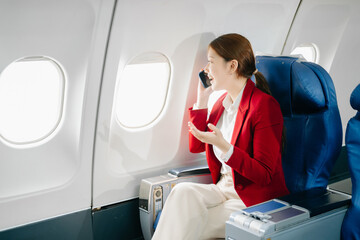 Young Asian executive excels in first class, multitasking with digital tablet, laptop and...