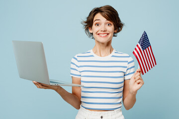 Young surprised IT woman wears striped t-shirt casual clothes hold American flag use work on laptop...