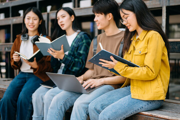 Young people college students is reading a book while relaxing sitting on grass in a campus park