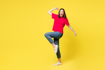Full body young woman she wears pink t-shirt casual clothes doing winner gesture celebrate clenching fists raise up leg isolated on plain yellow orange background studio portrait. Lifestyle concept.