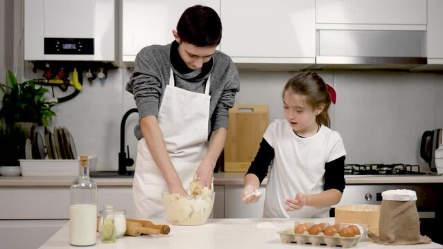 Cute funny children boy and girl learn kneading dough with hands having fun help happy parents in kitchen. Family kids brother and sister prepare cake cooking together at home