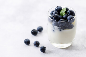 Ripe organic blueberries with yogurt in a glass on white stone table background. Selective focus.