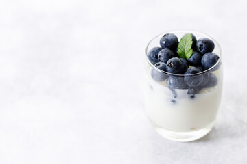 Ripe organic blueberries with yogurt in a glass on white stone table background. Selective focus.