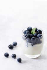 Ripe organic blueberries with yogurt in a glass on white stone table background. Selective focus.