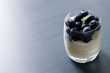 Ripe organic blueberries with yogurt in a glass on black stone table background. Selective focus.