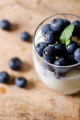 Ripe organic blueberries with yogurt in a glass on rustic wooden table background. Selective focus.