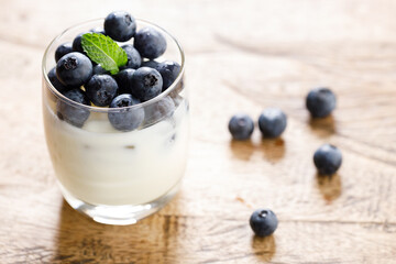 Ripe organic blueberries with yogurt in a glass on rustic wooden table background. Selective focus.