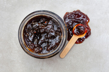 onion marmalade in a jar with spoon on light grey with copy space