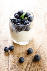 Ripe organic blueberries with yogurt in a glass on rustic wooden table background. Selective focus.