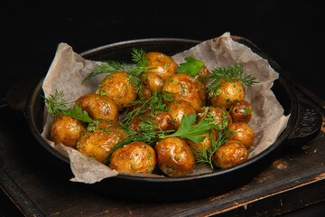 Potatoes fried country-style with parsley and dill, in a black cast iron skillet against a black background. Small-sized potatoes with skin