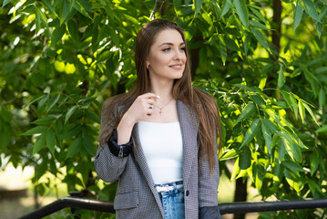 Pretty and attractive Caucasian young woman in stylish casual clothes posing with pleasure while walking in the park on a warm spring day. The concept of freedom, relax, style.