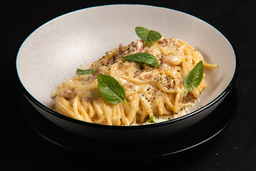 Carbonara pasta with basil, sauce, and cheese. Served in a gray plate against a black background
