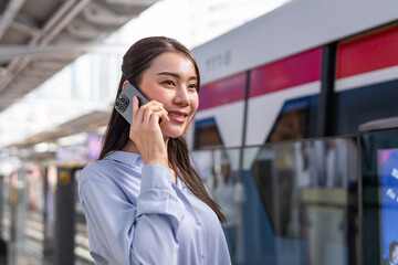 Asian woman talk on phone while waiting train at platform of metro station. 