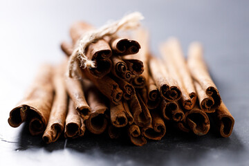 Cinnamon sticks dried tree bark spice on black stone table background. Selective focus.