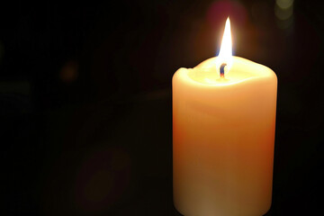A solitary white candle, lit with a small flame, against a dark black background.
