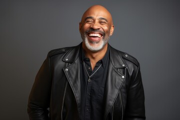 Obraz premium Portrait of a cheerful afro-american man in his 50s sporting a stylish leather blazer in minimalist or empty room background