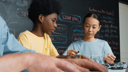 Young student fixing controller while teacher programing engineering code at STEM class. Closeup of...