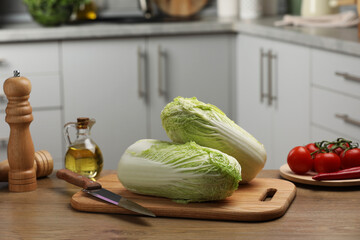 Fresh Chinese cabbages, knife, tomatoes and oil on wooden table in kitchen
