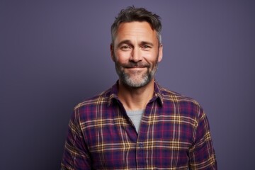 Portrait of a satisfied man in his 40s wearing a comfy flannel shirt in front of solid color backdrop