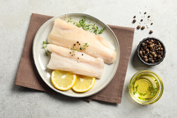 Plate with raw cod fish, spices, microgreens and lemon on grey textured table, flat lay