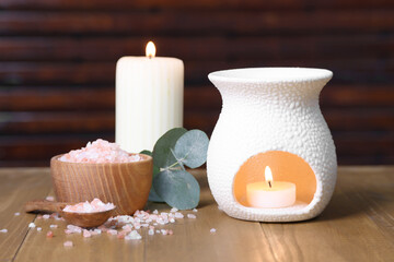 Different aromatherapy products, burning candles and eucalyptus leaves on wooden table