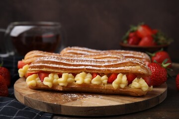 Delicious eclairs filled with cream and strawberries on wooden table