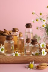 Aromatherapy. Different essential oils, flowers and almonds on pink background