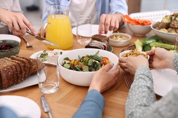 Friends eating vegetarian food at wooden table indoors, closeup