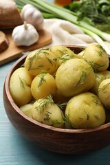 Tasty young boiled potatoes with dill in bowl on light blue wooden table