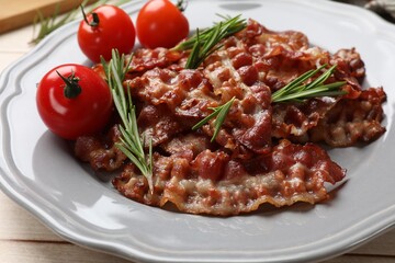 Slices of tasty fried bacon with rosemary and tomatoes on wooden table, closeup