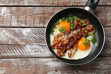 Tasty bacon, eggs and parsley in frying pan on wooden table, top view. Space for text