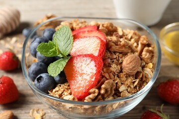 Tasty granola with berries, nuts and mint on wooden table, closeup