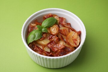 Delicious baked potatoes, bacon and basil in bowl on green background